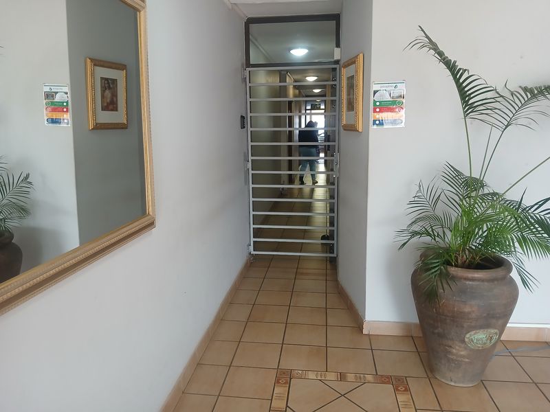 A commercial hallway featuring tiled flooring, recessed lighting, and a secure metal gate providing access to the interior corridor.