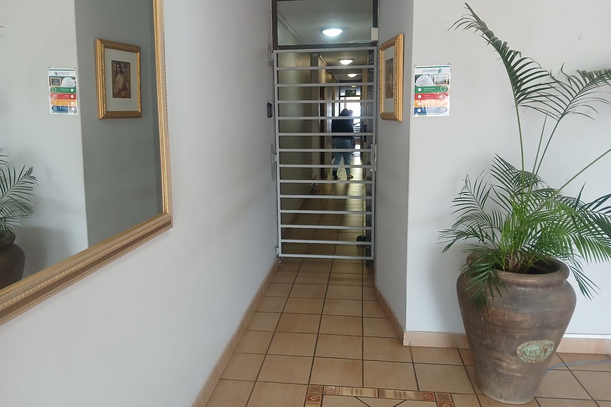 A commercial hallway featuring tiled flooring, recessed lighting, and a secure metal gate providing access to the interior corridor.