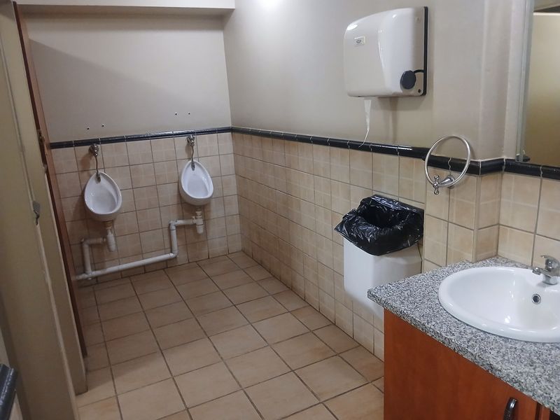 Commercial bathroom facility featuring two wall-mounted urinals, a vanity with a granite countertop, and tiled finishes throughout.