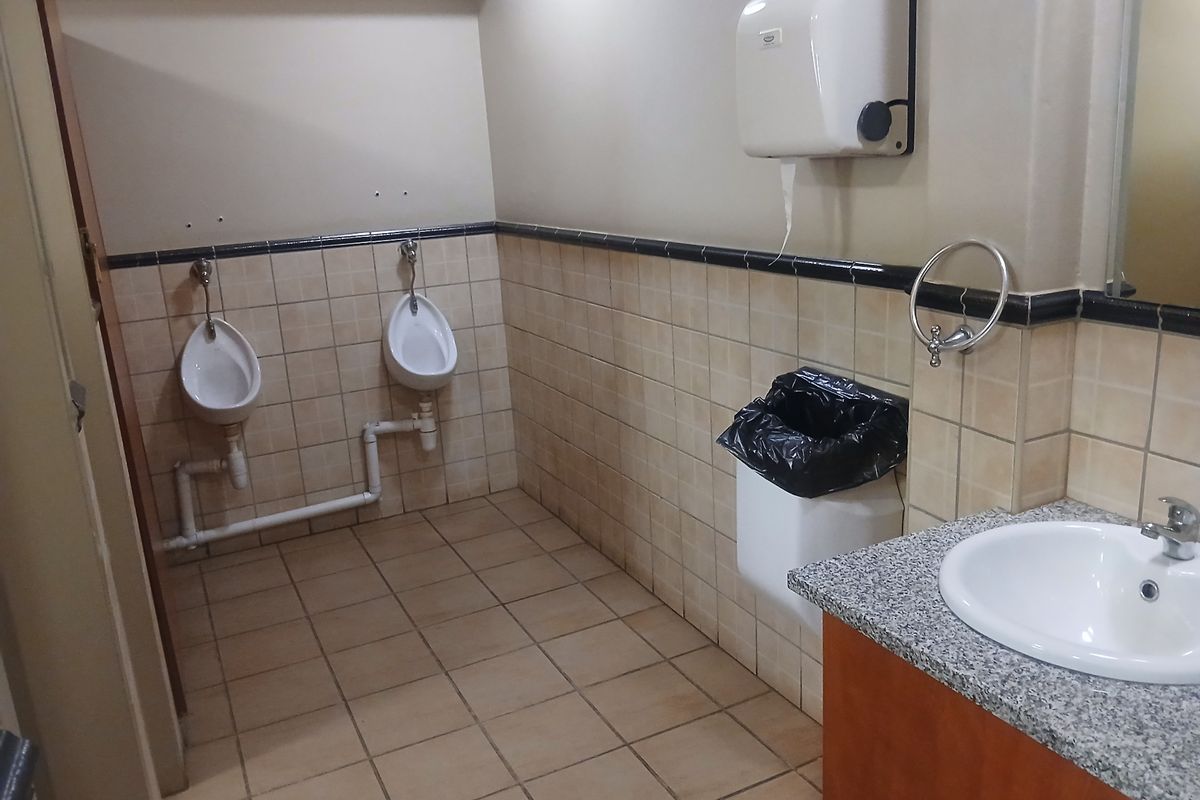 Commercial bathroom facility featuring two wall-mounted urinals, a vanity with a granite countertop, and tiled finishes throughout.
