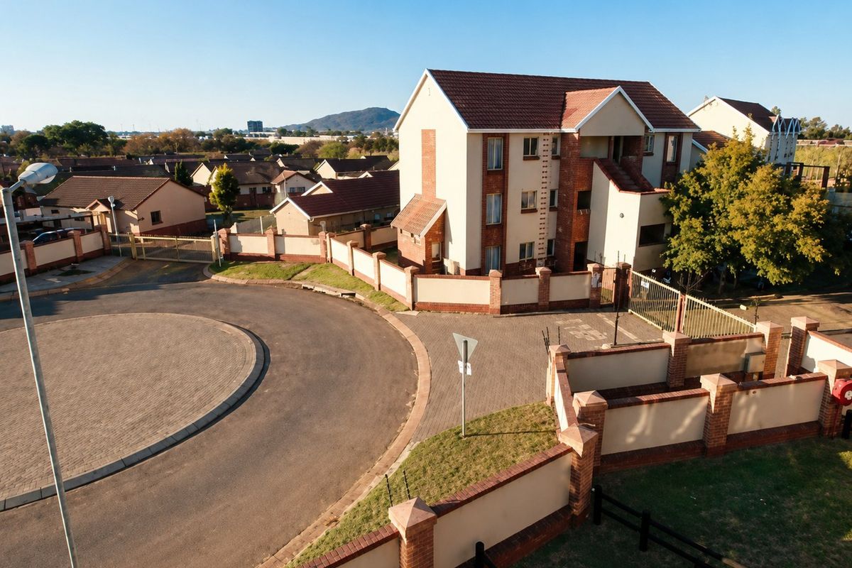 Aerial view of an apartment complex featuring a paved driveway, perimeter walling, and secure gated access within a residential estate.