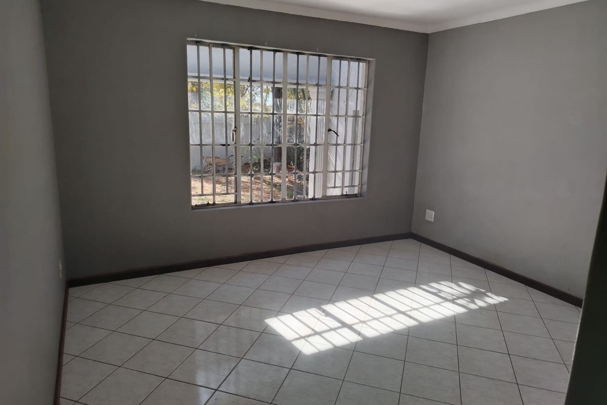 An empty bedroom featuring neutral grey walls, tiled flooring, and a window fitted with security bars.