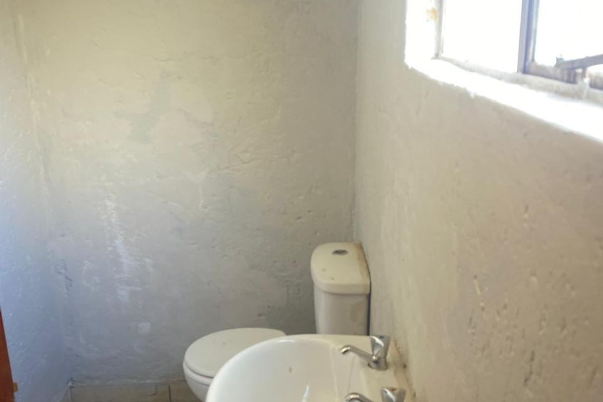 A small, basic bathroom featuring a pedestal basin and toilet with tiled flooring and plain wall finishes.