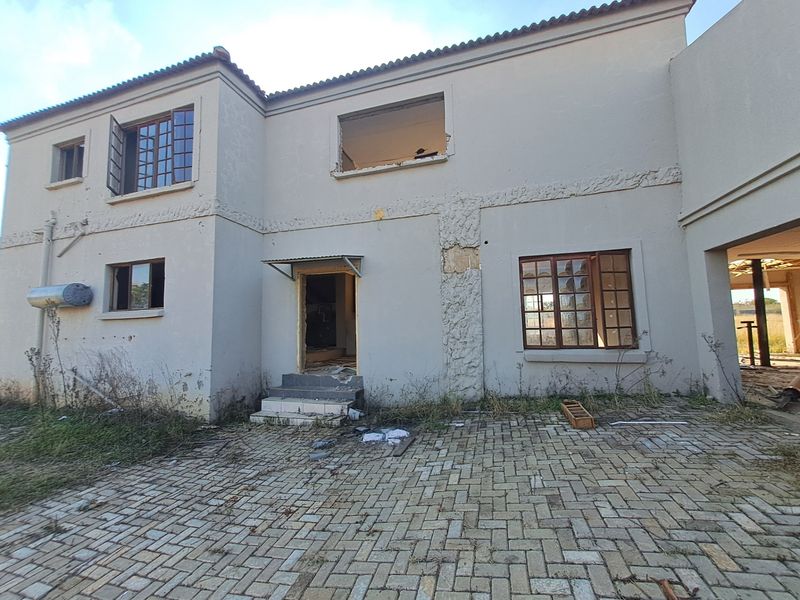 Rear elevation of a farm property showing significant structural wear, missing windows, and damaged exterior finishes requiring extensive renovation.