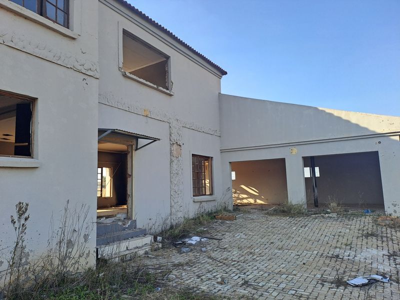 Rear view of a farm property featuring a paved courtyard, multi-car garage, and a two-story structure requiring significant exterior maintenance and restoration.