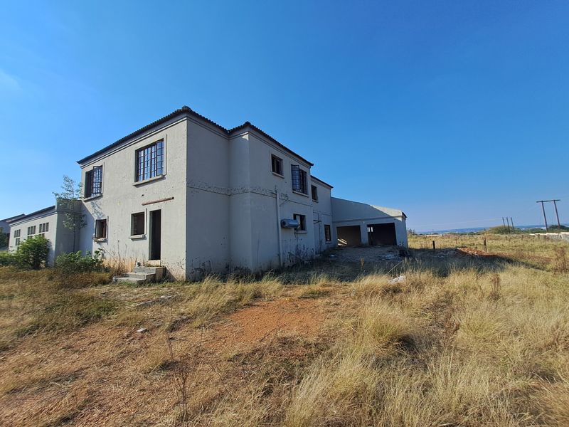 Rear view of a double-storey farmhouse structure showing significant exterior wear, peeling paint, and an attached garage on a large rural plot.