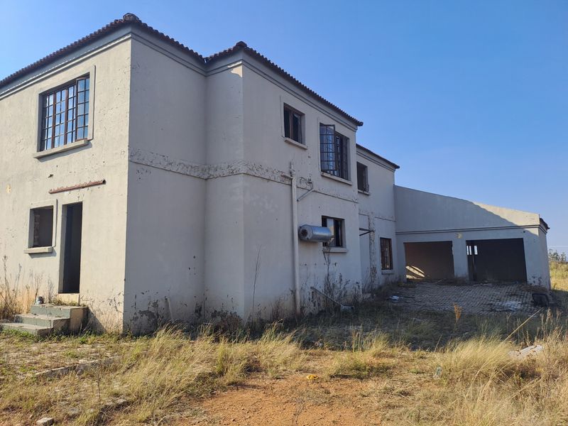 Rear view of a two-story farmhouse showing significant exterior wear, including peeling paint, cracked plaster, and an attached garage structure.