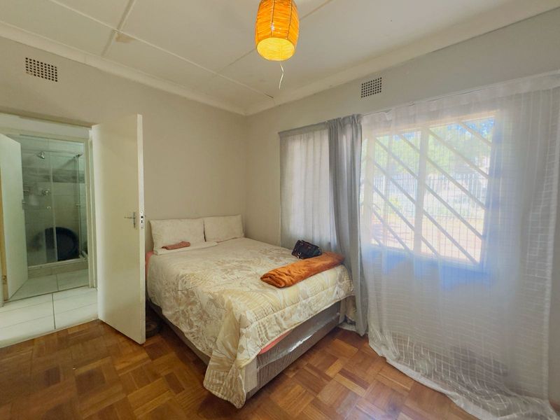 A bedroom featuring parquet flooring, security bars on the window, and direct access to an en-suite bathroom.
