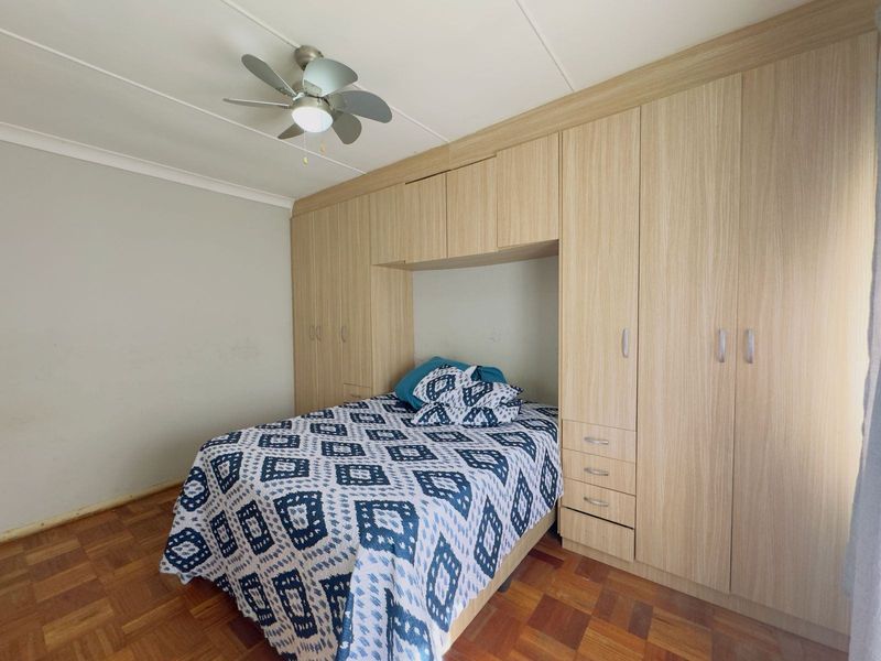 A bedroom featuring extensive light wood built-in cabinetry, a ceiling fan, and traditional parquet flooring.