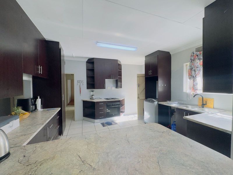 A functional kitchen featuring dark wood cabinetry, stone-look laminate countertops, built-in oven and hob, and tiled flooring with ample workspace.