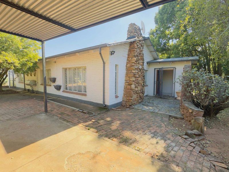 Rear exterior view of the house featuring a stone chimney, brick paved patio area, and a covered carport structure.