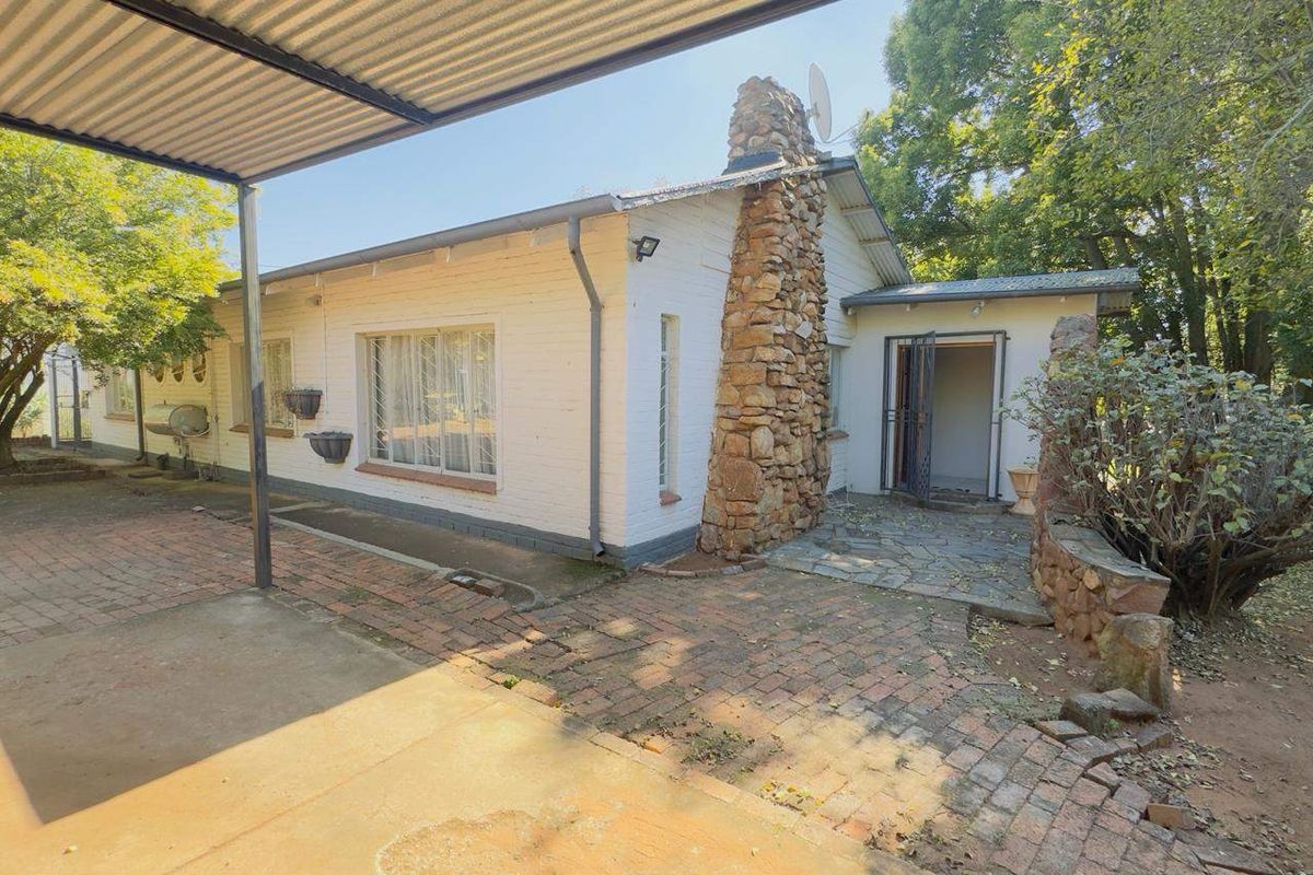 Rear exterior view of the house featuring a stone chimney, brick paved patio area, and a covered carport structure.