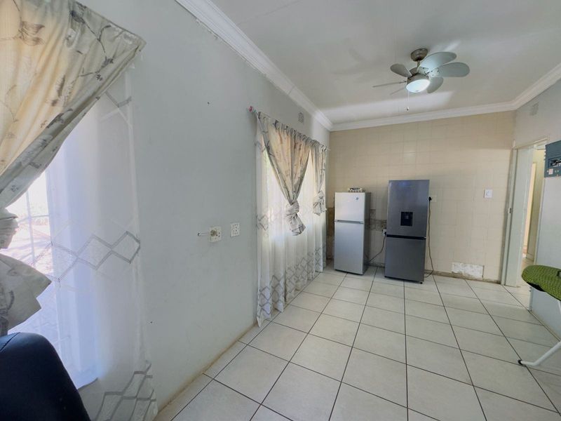 A sparse kitchen area featuring tiled flooring, a ceiling fan, and tiled wall sections, currently requiring cosmetic repairs to the wall finishes.