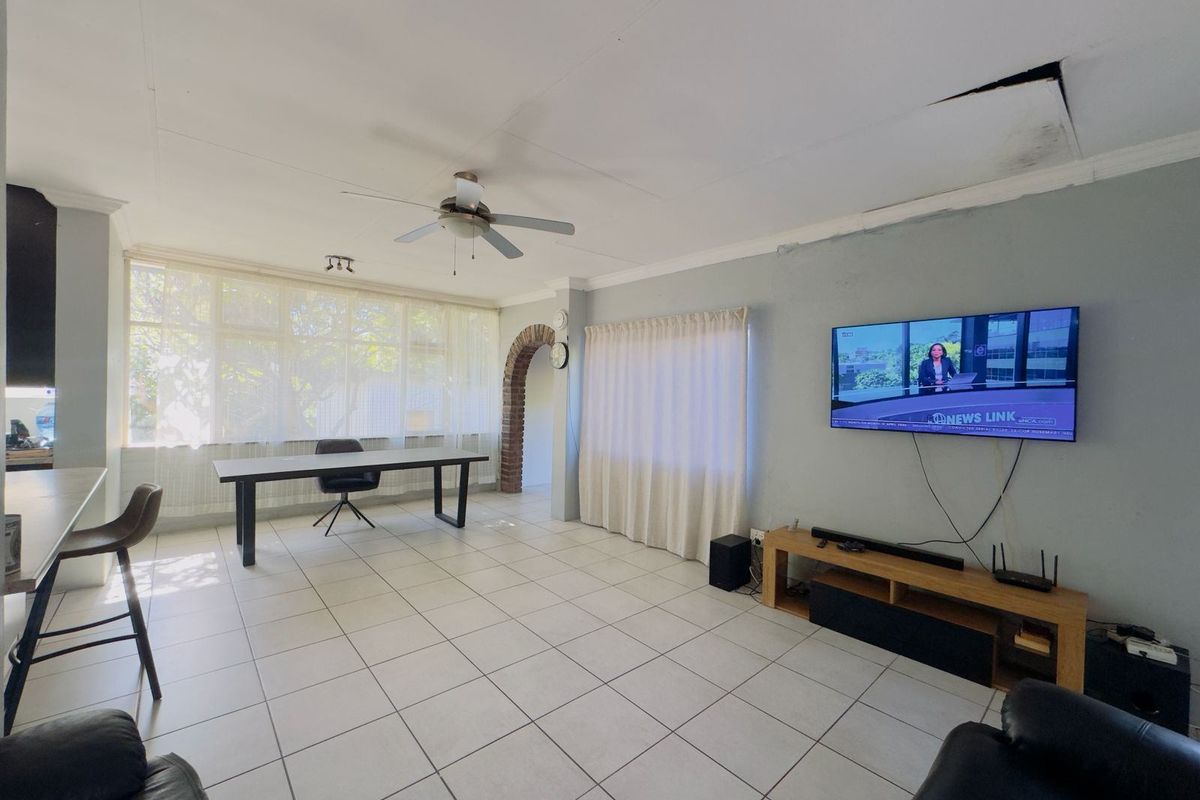 Spacious living area featuring tiled flooring, a ceiling fan, and a distinctive brick archway, requiring some ceiling and wall maintenance.