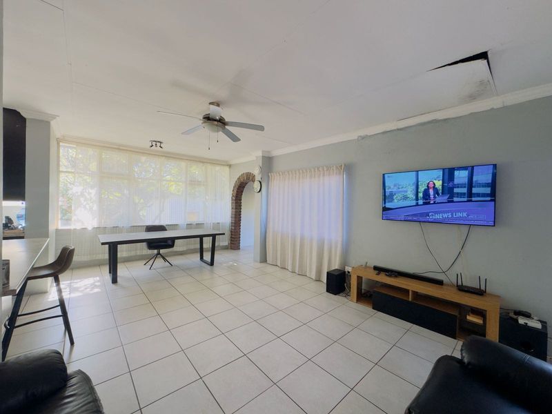 Spacious living area featuring tiled flooring, a ceiling fan, and a distinctive brick archway, requiring some ceiling and wall maintenance.