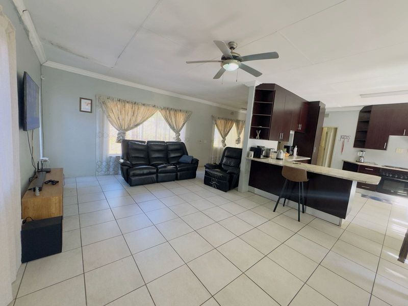 Open-plan living and kitchen area featuring tiled floors, dark wood cabinetry, stone countertops, and a ceiling fan.