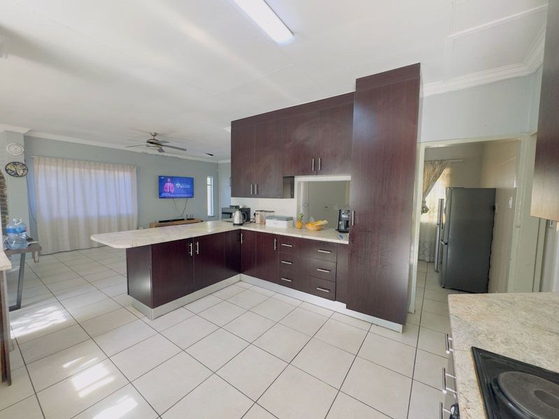 Open-plan kitchen featuring dark wood cabinetry, stone countertops, and a breakfast bar, seamlessly flowing into the adjacent living area with tiled flooring throughout.