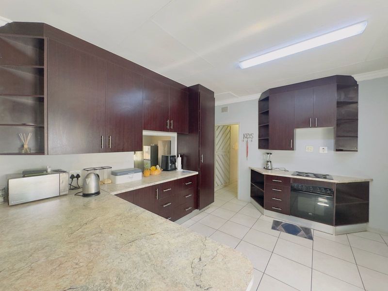 A functional kitchen featuring dark wood-finish cabinetry, stone-look laminate countertops, built-in oven, hob, and tiled flooring.