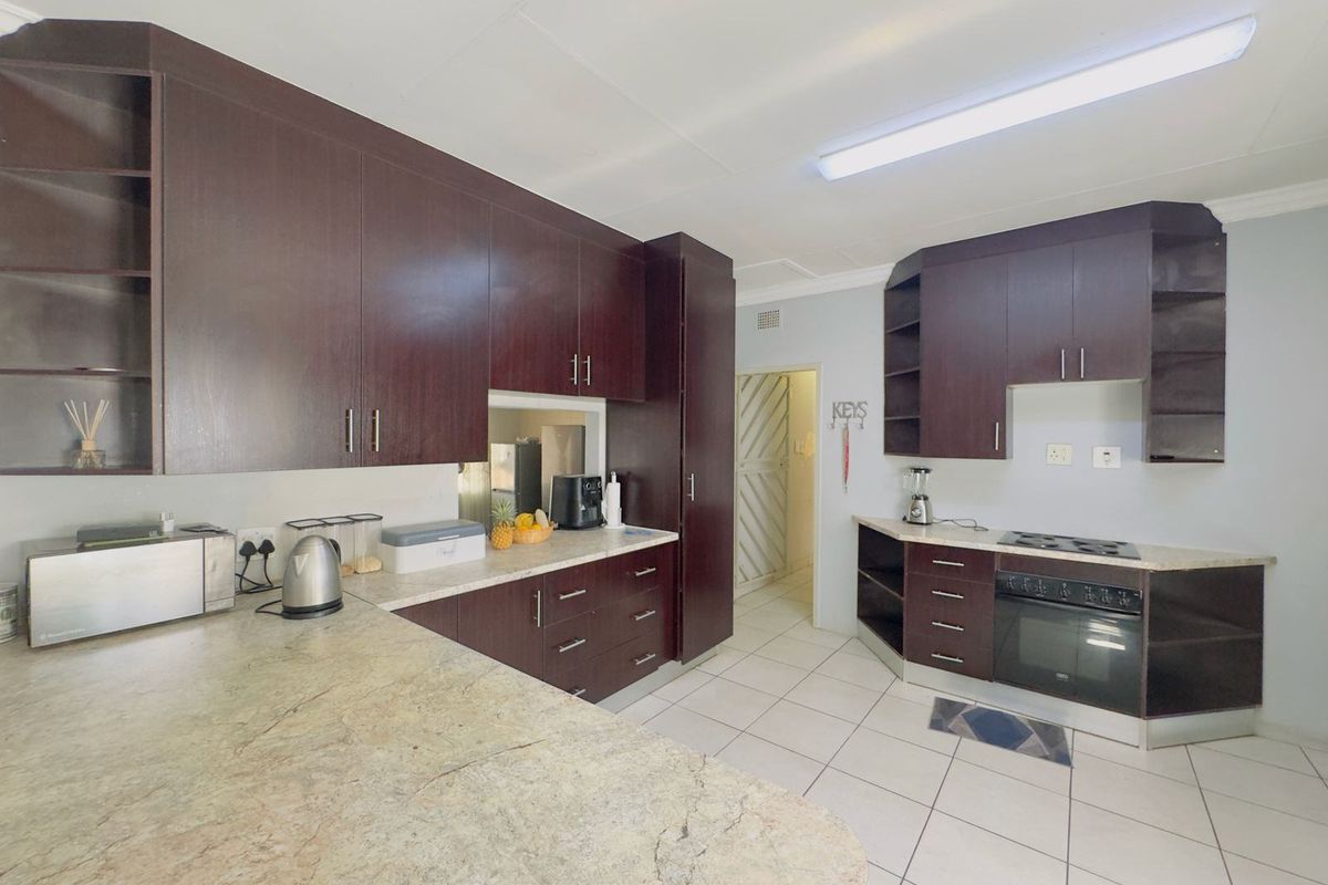 A functional kitchen featuring dark wood-finish cabinetry, stone-look laminate countertops, built-in oven, hob, and tiled flooring.