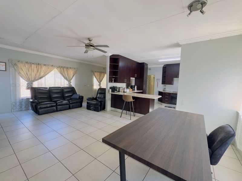 Open-plan living and kitchen area featuring tiled flooring, a breakfast bar, and dark wood cabinetry, with a ceiling fan and coved cornicing.