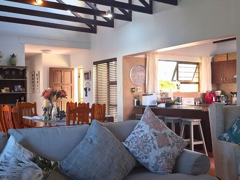 Open-plan living and dining area featuring exposed timber ceiling beams, flowing into a functional kitchen with granite countertops and warm timber cabinetry.