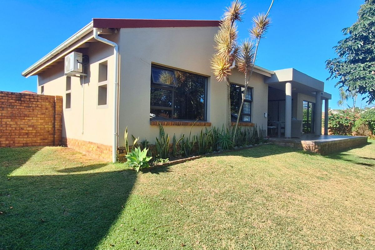 Rear view of the townhouse featuring a covered patio, brick boundary wall, and well-maintained lawn area.