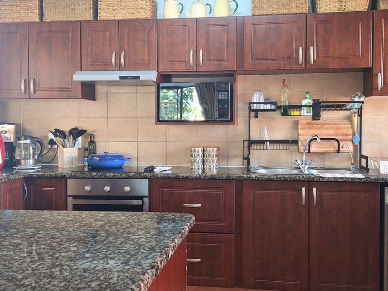 A functional kitchen featuring dark wood cabinetry, granite countertops, a built-in oven, extractor fan, and a tiled backsplash.