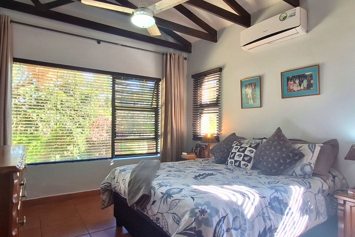 A cozy bedroom featuring exposed timber ceiling beams, tiled flooring, and a wall-mounted split-system air conditioner, offering a comfortable and functional living space.