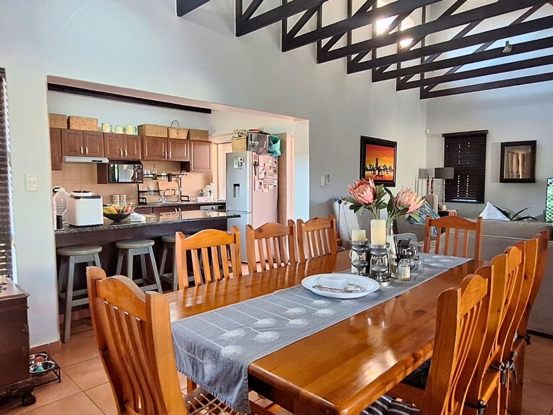 Open-plan living and dining area featuring exposed timber beams, tiled flooring, and a functional kitchen with granite countertops and built-in cabinetry.