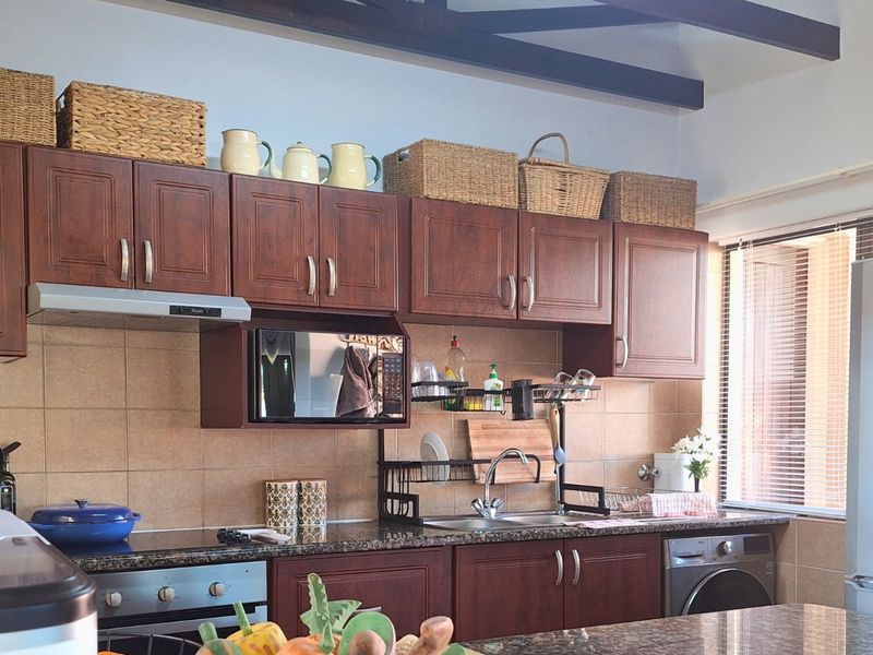 A functional kitchen featuring dark wood cabinetry, granite countertops, a tiled backsplash, and exposed ceiling beams, providing a classic and practical cooking space.