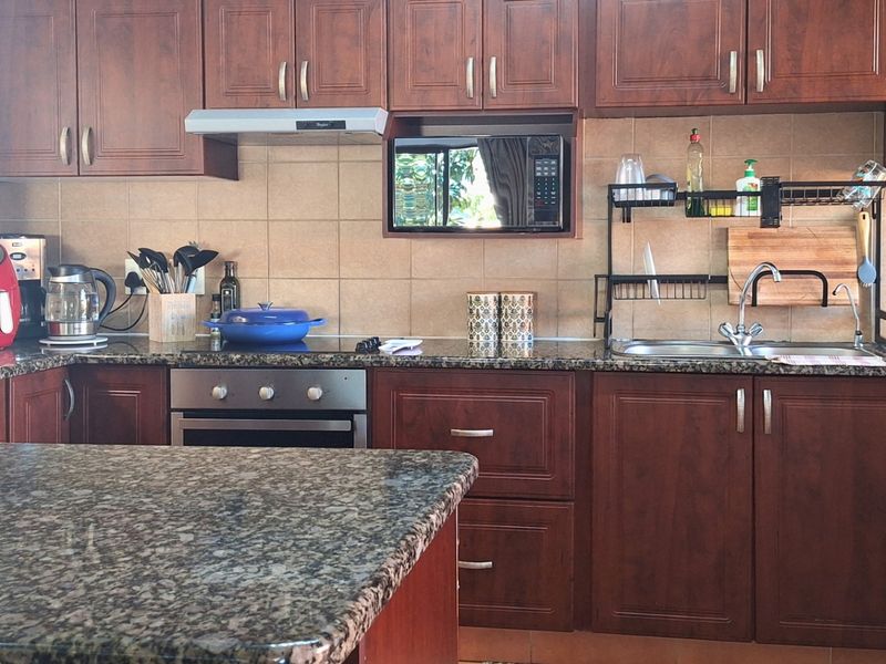 A functional kitchen featuring dark wood cabinetry, granite countertops, a built-in oven, and a tiled backsplash with integrated microwave and extractor fan.