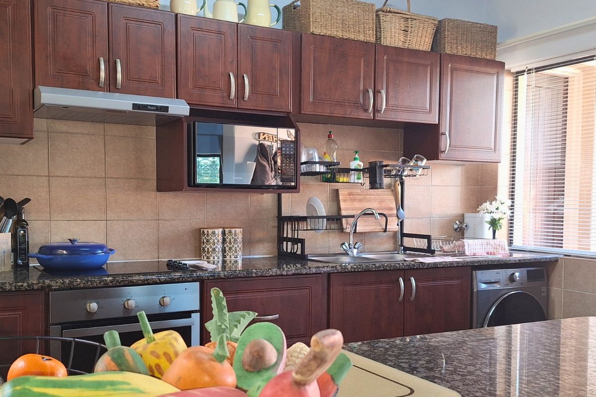 A functional kitchen featuring dark wood cabinetry, granite countertops, tiled backsplash, and integrated appliances including an oven, extractor fan, and washing machine.