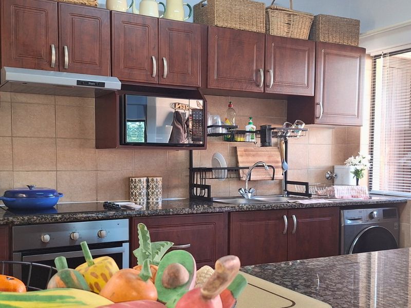 A functional kitchen featuring dark wood cabinetry, granite countertops, tiled backsplash, and integrated appliances including an oven, extractor fan, and washing machine.