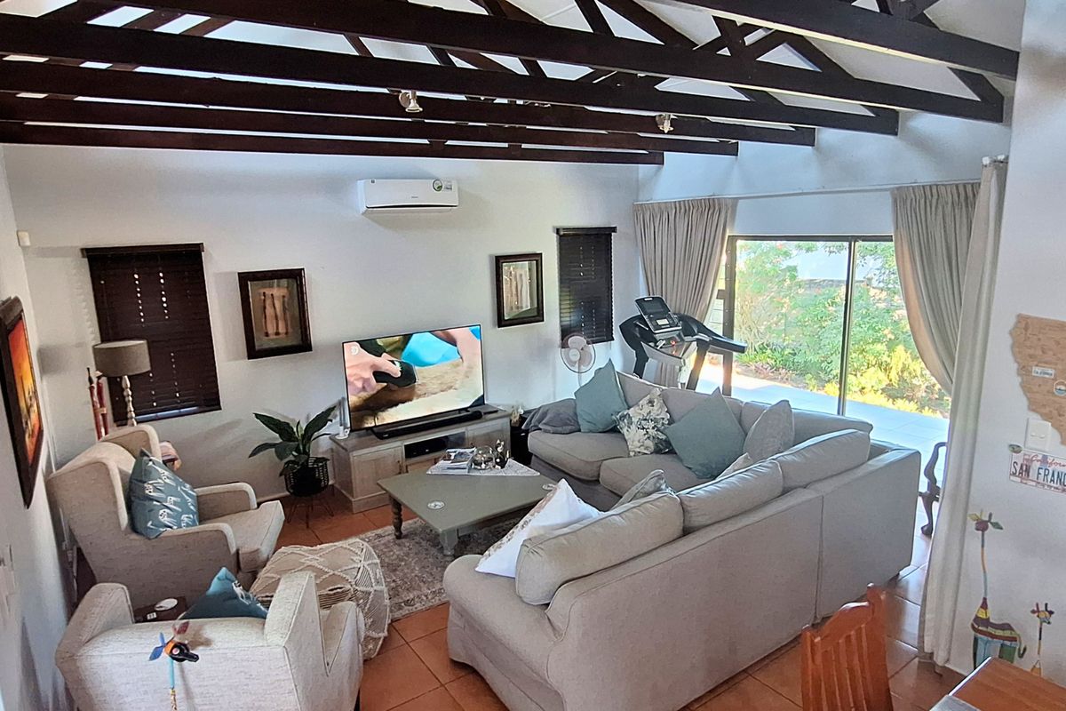 Spacious living room featuring exposed timber ceiling beams, tiled flooring, and large sliding glass doors providing natural light and access to the outdoor area.