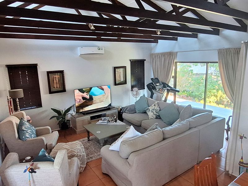 Spacious living room featuring exposed timber ceiling beams, tiled flooring, and large sliding glass doors providing natural light and access to the outdoor area.