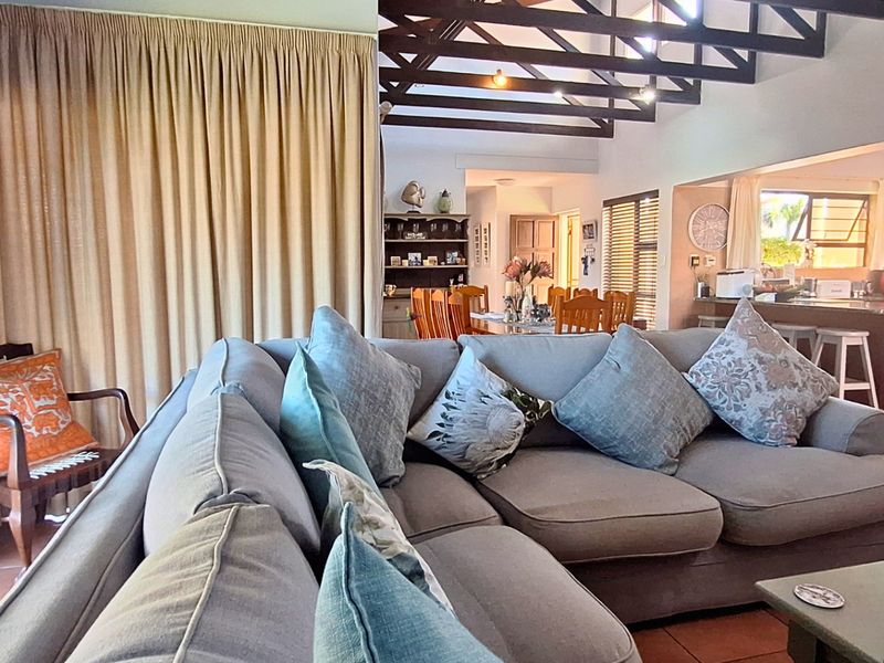 Spacious open-plan living area featuring exposed timber roof trusses, tiled flooring, and a functional kitchen with a breakfast bar.