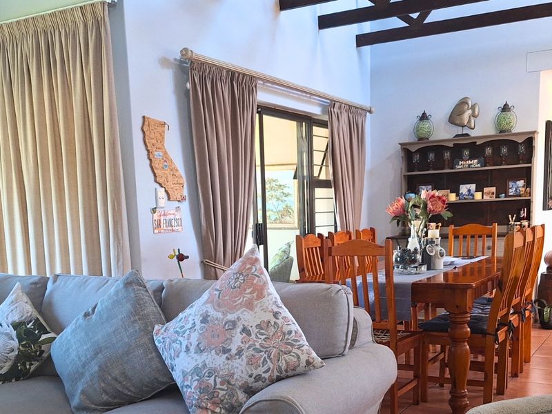 Open plan living and dining area featuring exposed timber ceiling beams, tiled flooring, and sliding glass doors leading to an outdoor patio.