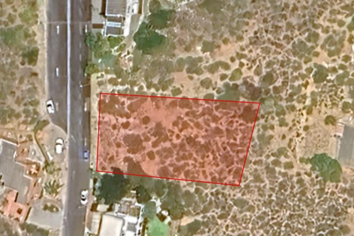 An aerial view of a vacant residential plot highlighted in red, showing the surrounding neighborhood and natural vegetation.