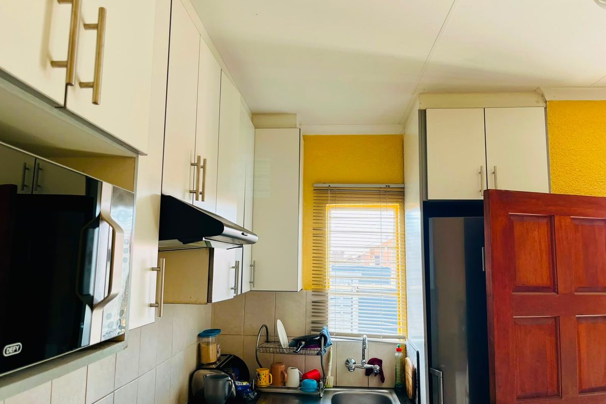 Compact kitchen featuring white cabinetry, dark countertops, a built-in microwave, extractor fan, and a stainless steel sink with a window view.