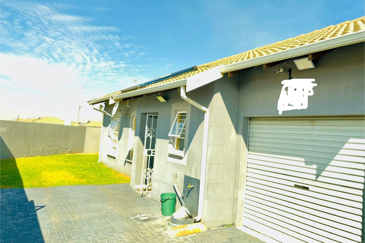 Rear exterior view of the property featuring a paved area, lawn, roller garage door, and security gate access.