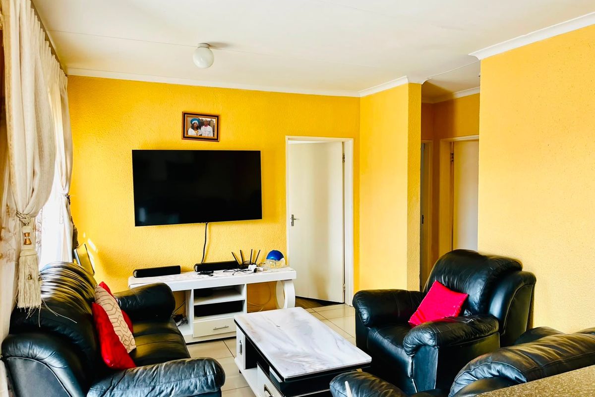 A bright living room featuring tiled flooring, coved ceilings, and yellow textured walls, providing a functional and well-lit space for relaxation.