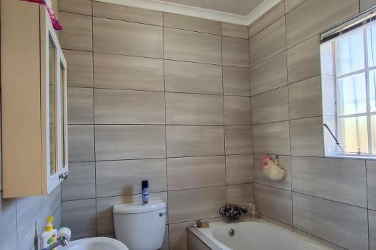 A functional bathroom featuring full-height wall tiling, a built-in vanity cabinet, a standard toilet, and a bathtub with a window for natural light.