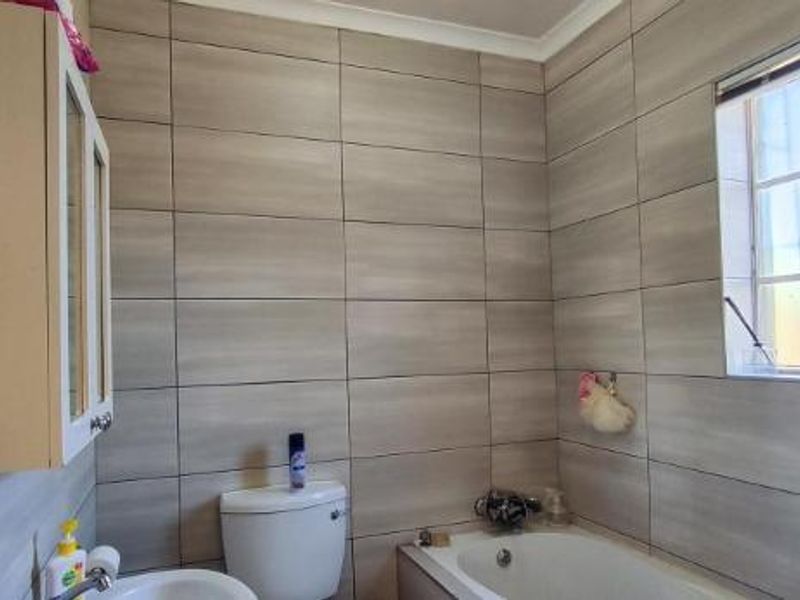 A functional bathroom featuring full-height wall tiling, a built-in vanity cabinet, a standard toilet, and a bathtub with a window for natural light.