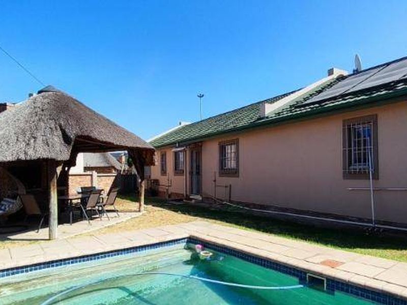 Rear garden area featuring a swimming pool with solar heating panels and a traditional thatched lapa for outdoor entertainment.