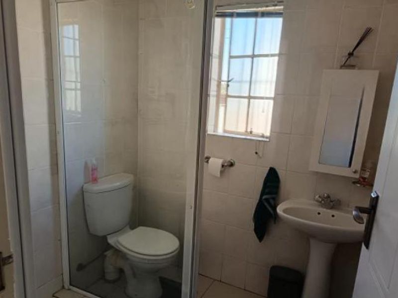 A functional bathroom featuring a shower enclosure, pedestal basin, and toilet with tiled finishes throughout.