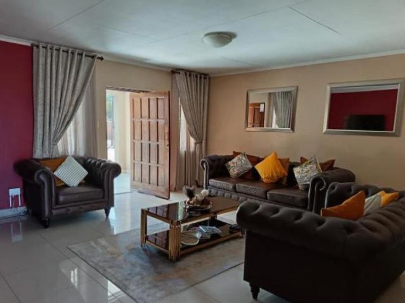 A spacious living room featuring tiled flooring, a feature wall, and direct access to an outdoor area through a timber door.