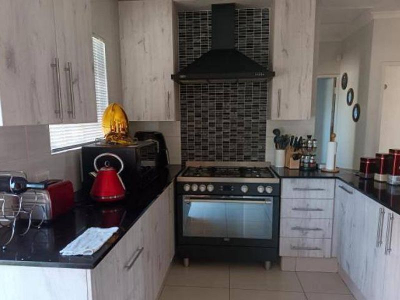Modern kitchen featuring light wood-grain cabinetry, black granite countertops, a gas stove with an extractor fan, and a decorative mosaic tiled backsplash.
