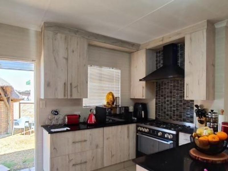 A functional kitchen featuring light wood-grain cabinetry, dark granite countertops, a gas hob with extractor fan, and a tiled backsplash, with direct outdoor access.