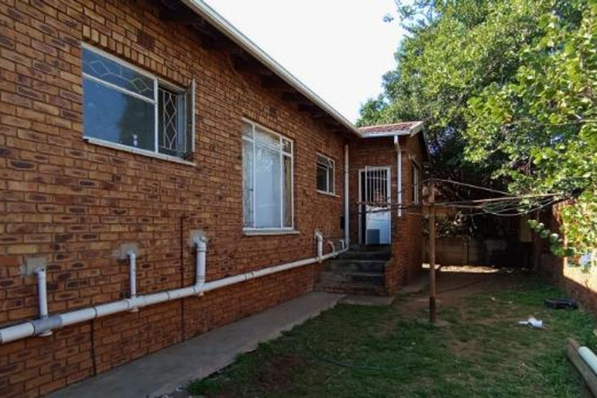 Rear exterior view of the house featuring exposed brick walls, external plumbing infrastructure, and a small concrete staircase leading to a rear entrance.