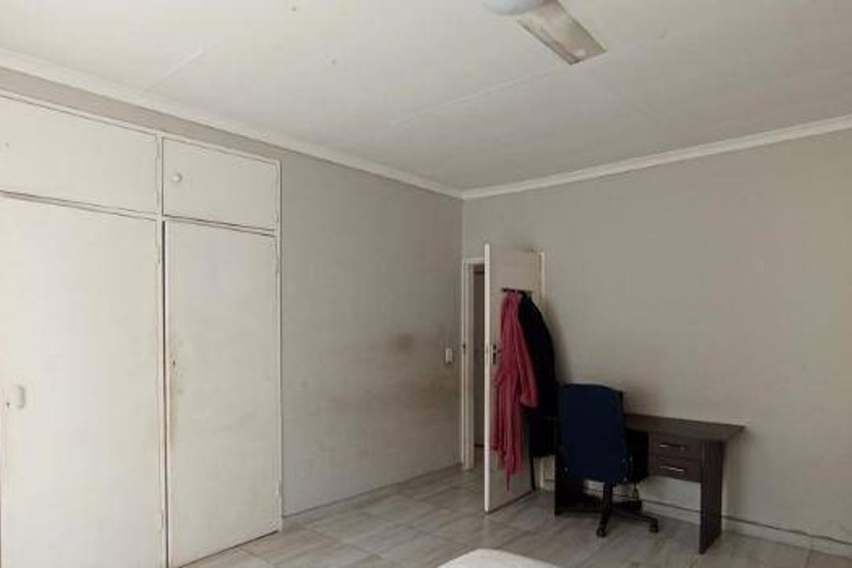 A bedroom featuring built-in cupboards, tiled flooring, and a ceiling fan, requiring cosmetic updates to the walls and finishes.